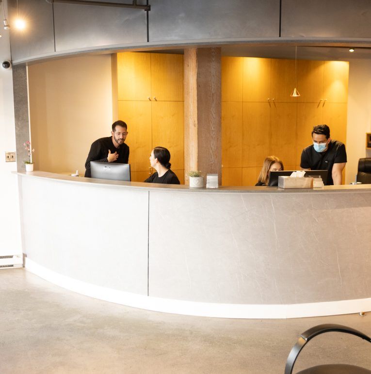 The front desk at Yaletown Dentistry, staff at work beneath oak cabinetry