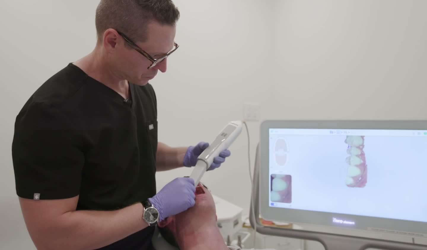 An intraoral scan on the monitor, gloved hands on the scanner